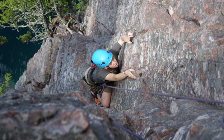 A person wearing safety gear is secured by ropes as they climb up a rock wall towards the camera.